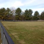 Two community service volunteers help to clean up the baseball field at New Lexington High School.