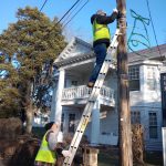 Two community service volunteers remove old Christmas lights from a telephone pole in New Straitsville.