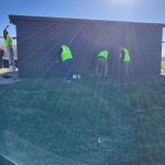 Four community service member repaint the dugout on the New Lexington High School softball field.