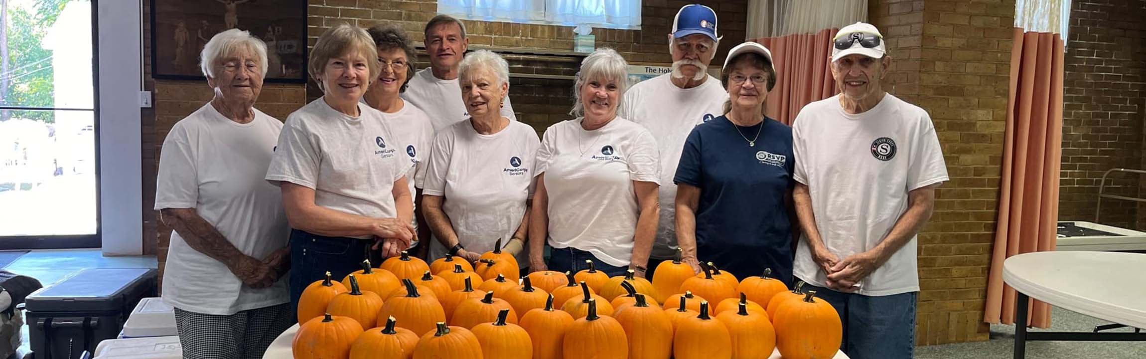 Group of senior citizens gathered around a table with many pumpkins